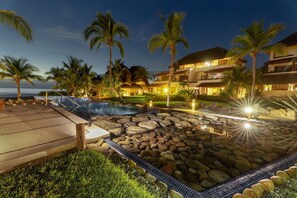 Um resort com piscina, palmeiras e vista para o oceano.