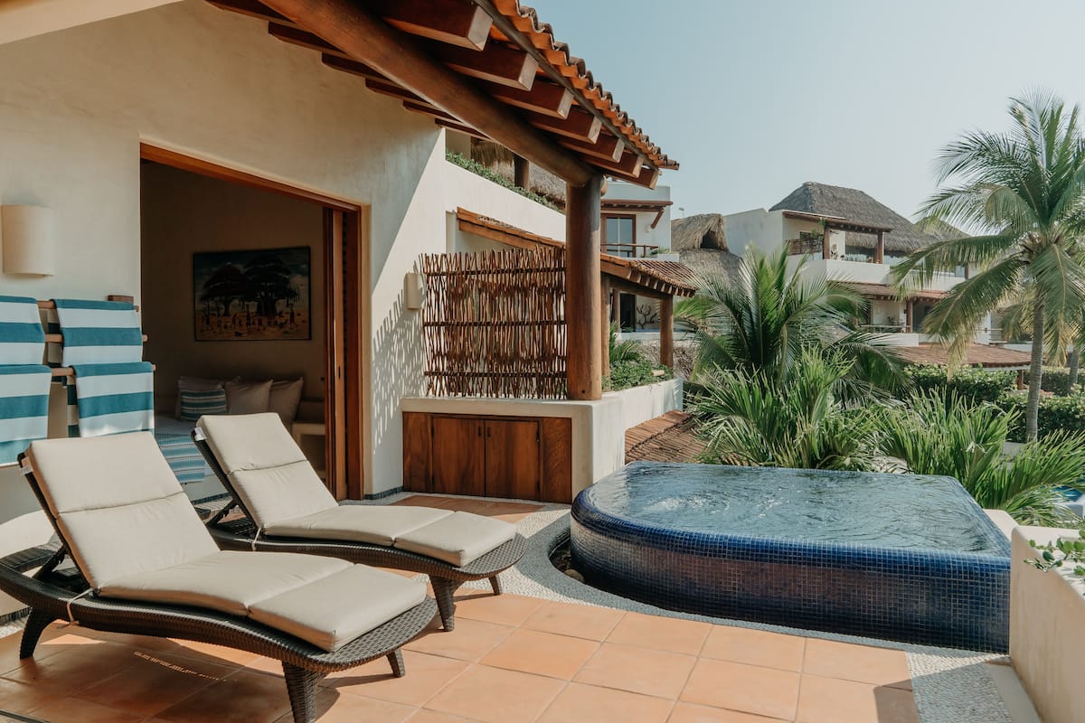 Un área de piscina con sillones reclinables, una bañera de hidromasaje y vistas a un edificio de resort.