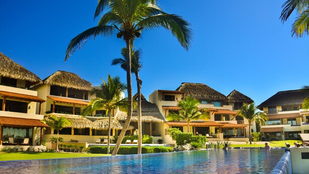 Un resort con piscina, edificios de techo de paja y palmeras.