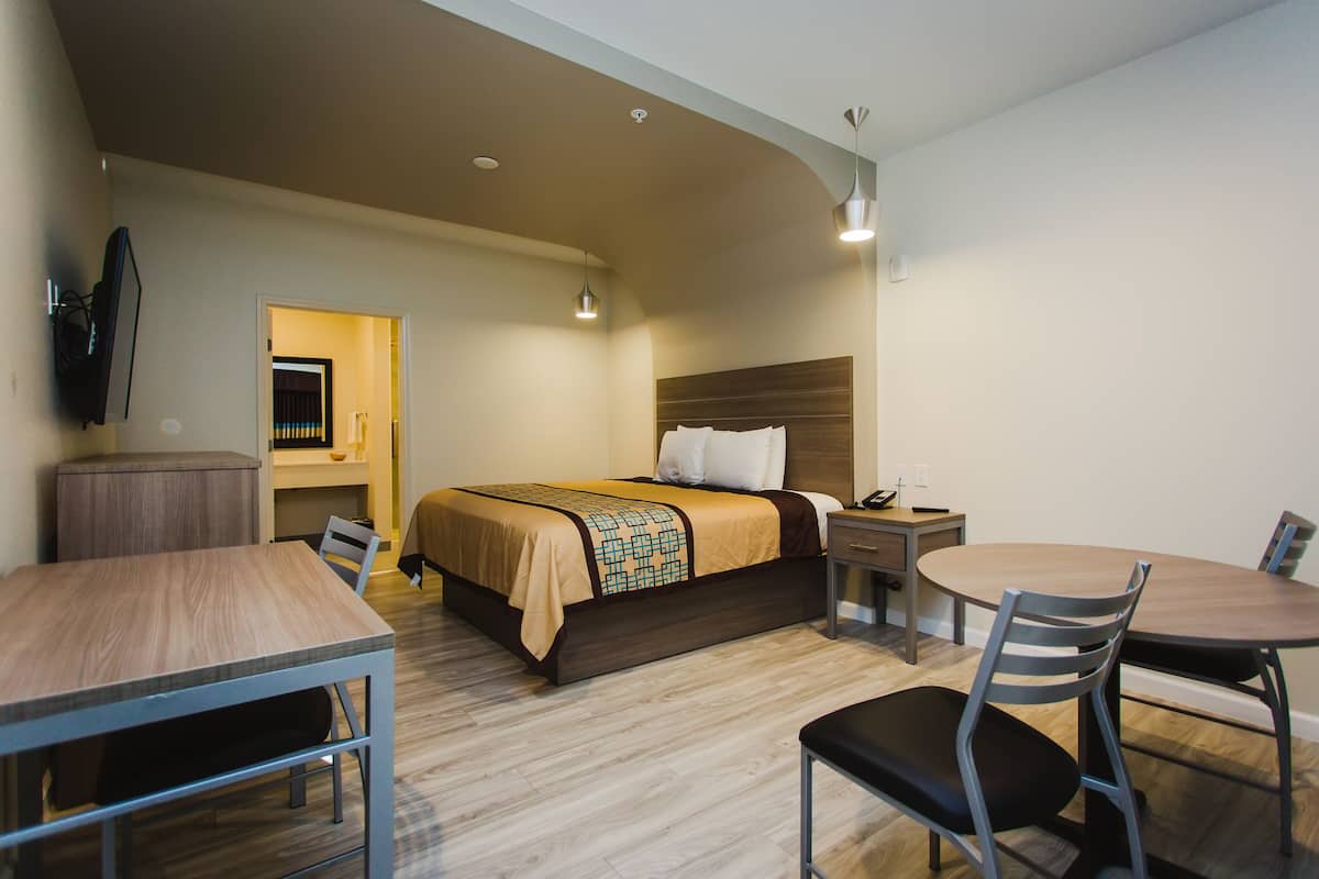 A hotel room with a bed, a desk, a chair, a table, and a TV.