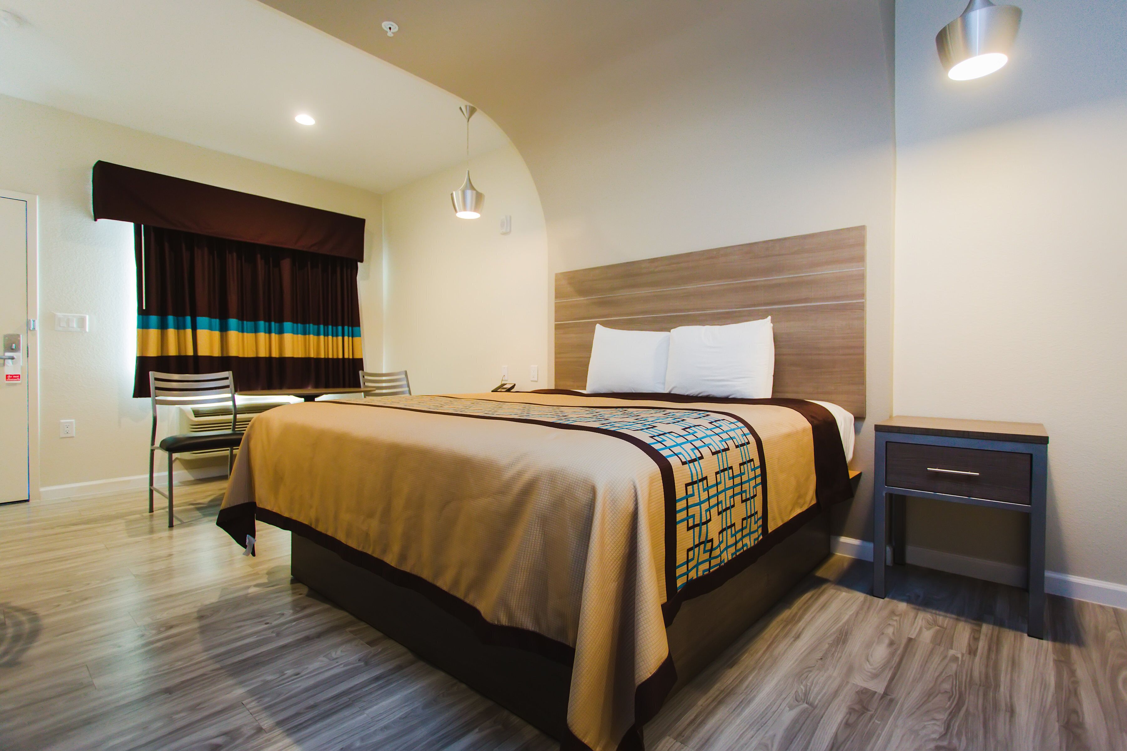 Une chambre d’hôtel avec un lit, une table de chevet, une chaise et une fenêtre avec des rideaux.
