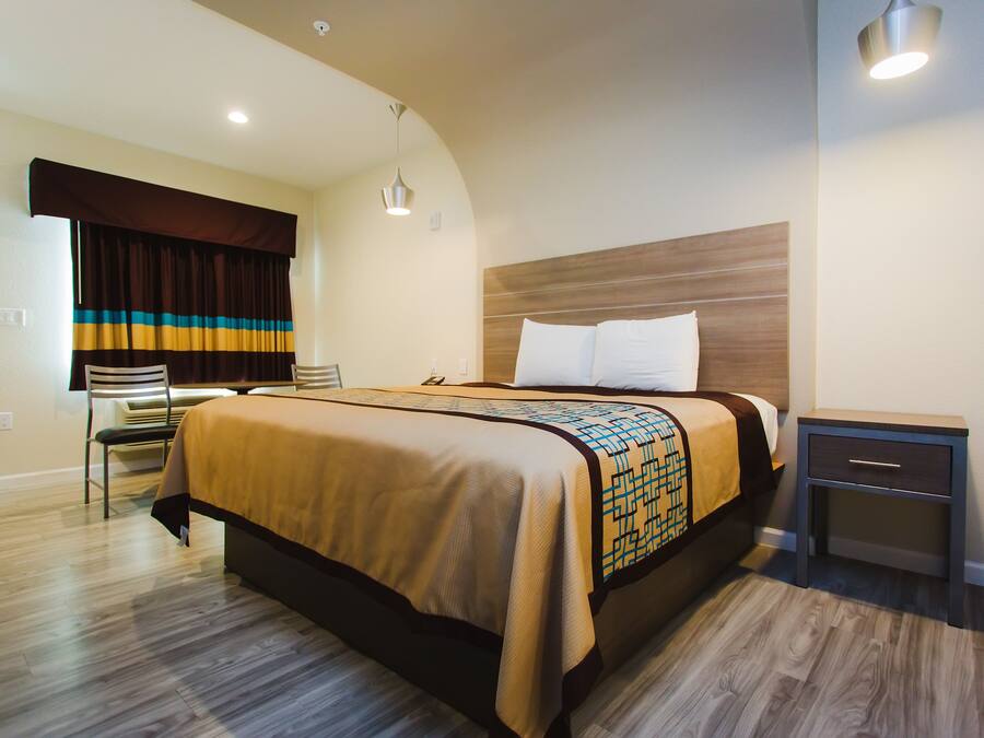 Une chambre d’hôtel avec un lit, une table de chevet, une chaise et une fenêtre avec des rideaux.