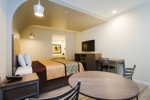 A hotel room with a bed, bedside table, desk, chair, and a TV. - Scottish Inns & Suites Atascocita (Humble)