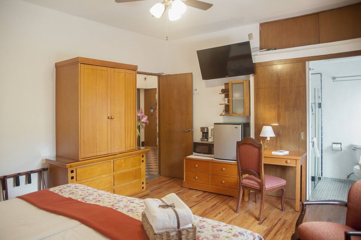 A bedroom with a bed, wooden wardrobe, desk, chair, and a television.