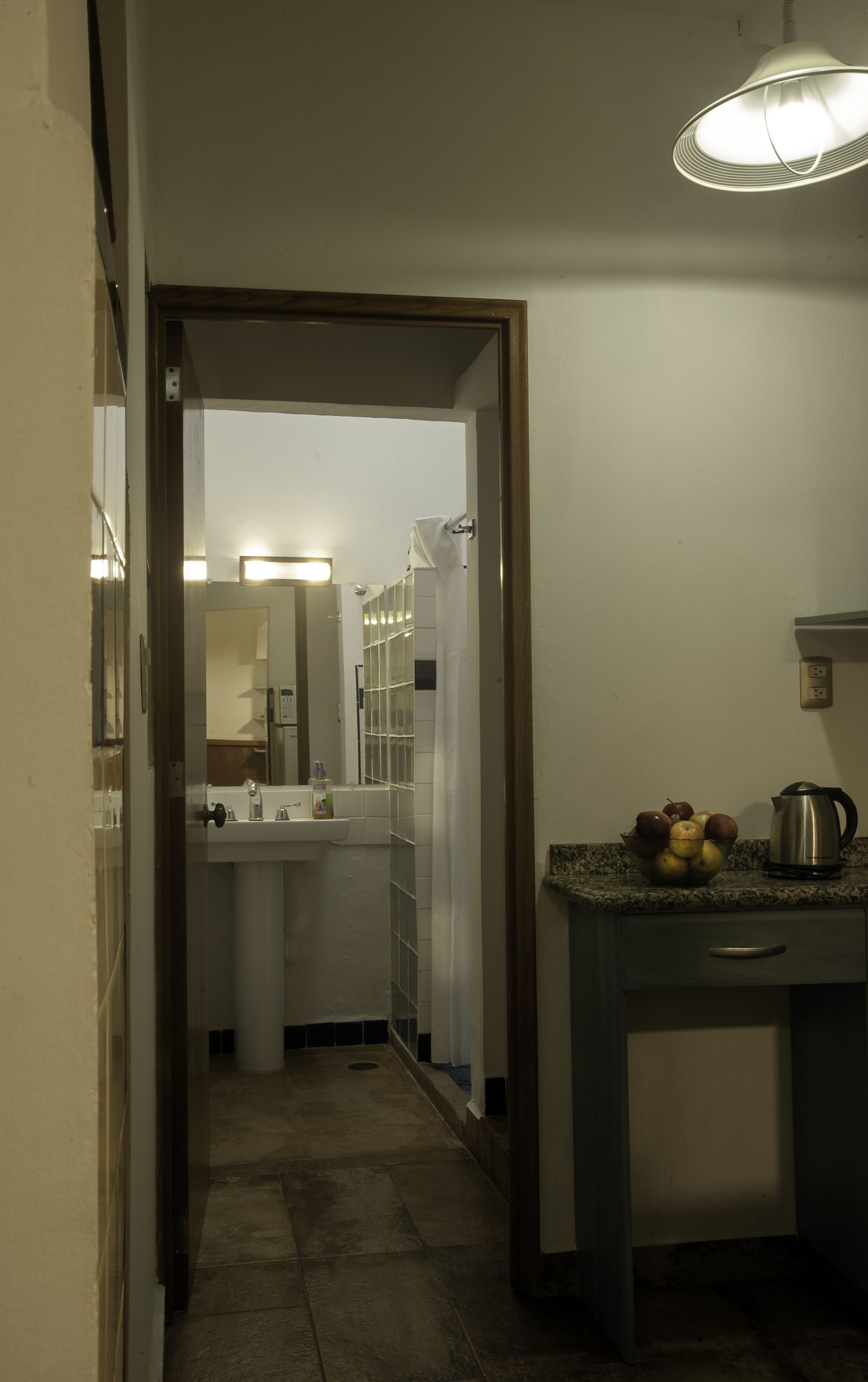 A narrow hallway with a sink, mirror, and a fruit bowl on a counter.