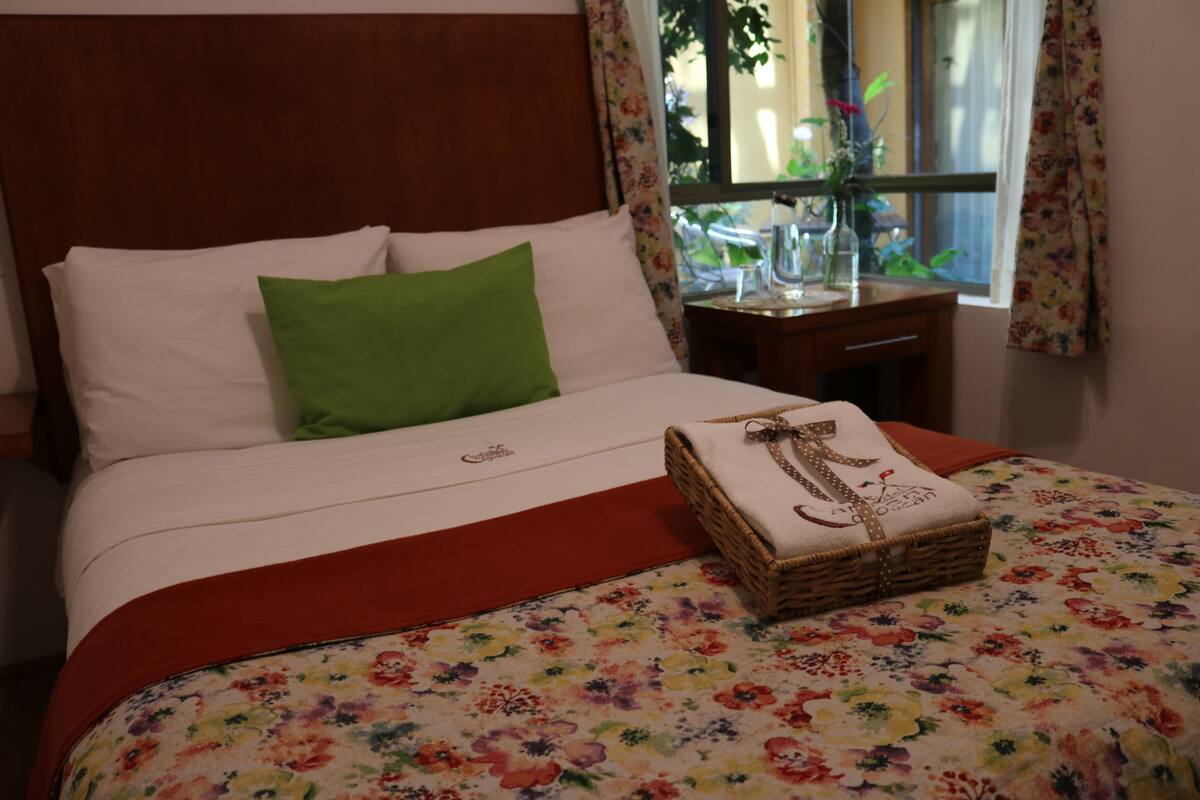 A neatly made bed with a floral bedspread, a green pillow, and a basket with a cloth.