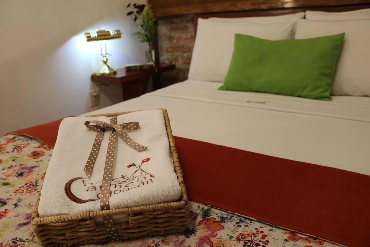 A neatly made bed with a green pillow, a decorative towel with a ribbon, and a lamp on a bedside table.