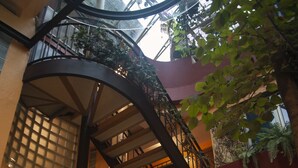 Un atrio de varios niveles con una escalera en espiral, plantas en macetas y vistas al cielo a través de un techo de cristal.