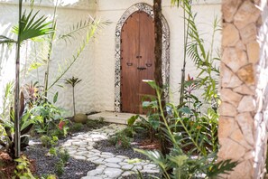 A stone pathway leading to a wooden door with a decorative arch, surrounded by various plants and greenery. - Villas Las Palmas (La Fortuna)