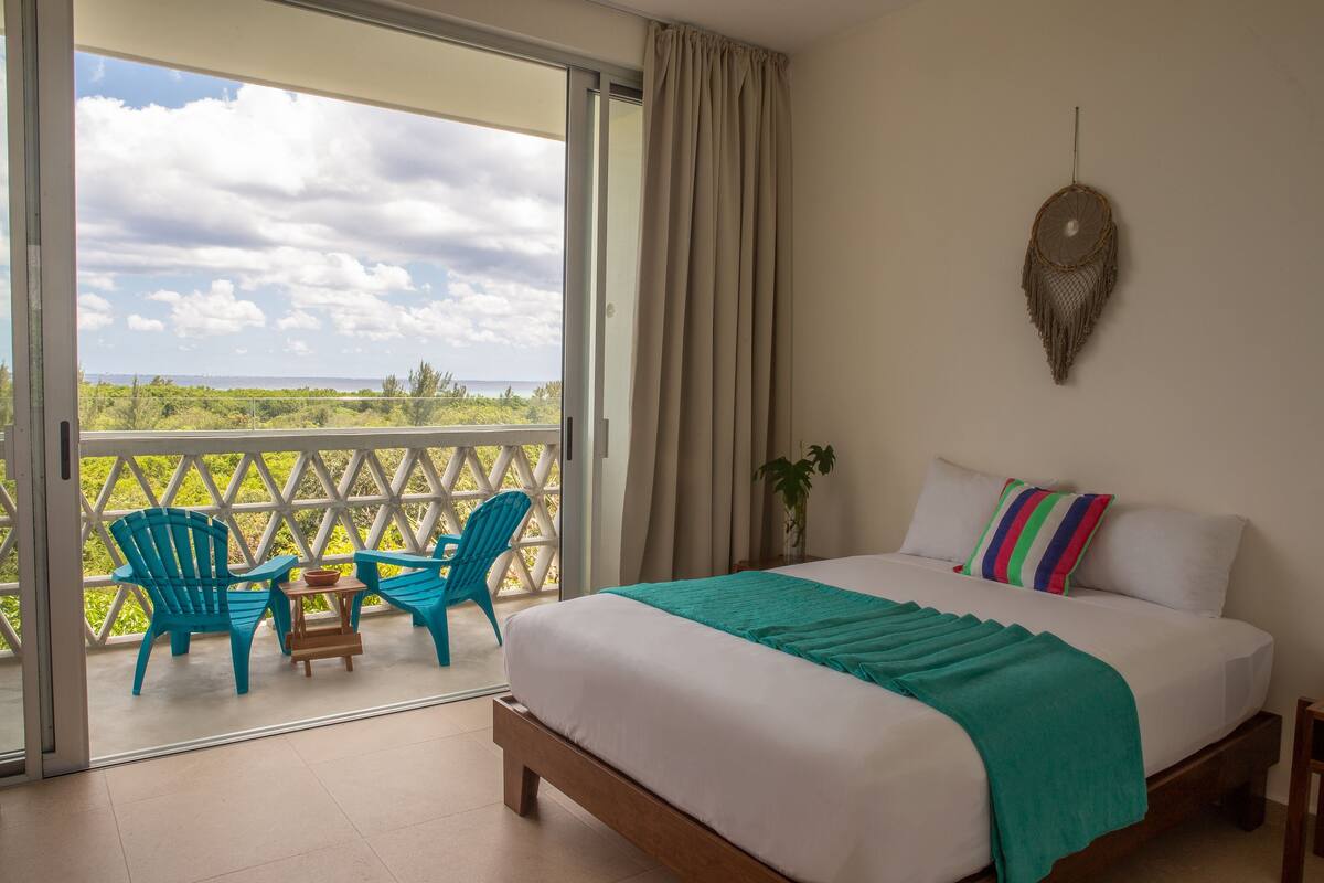 Une chambre avec un grand lit, une vue sur l’extérieur et un balcon avec des chaises.