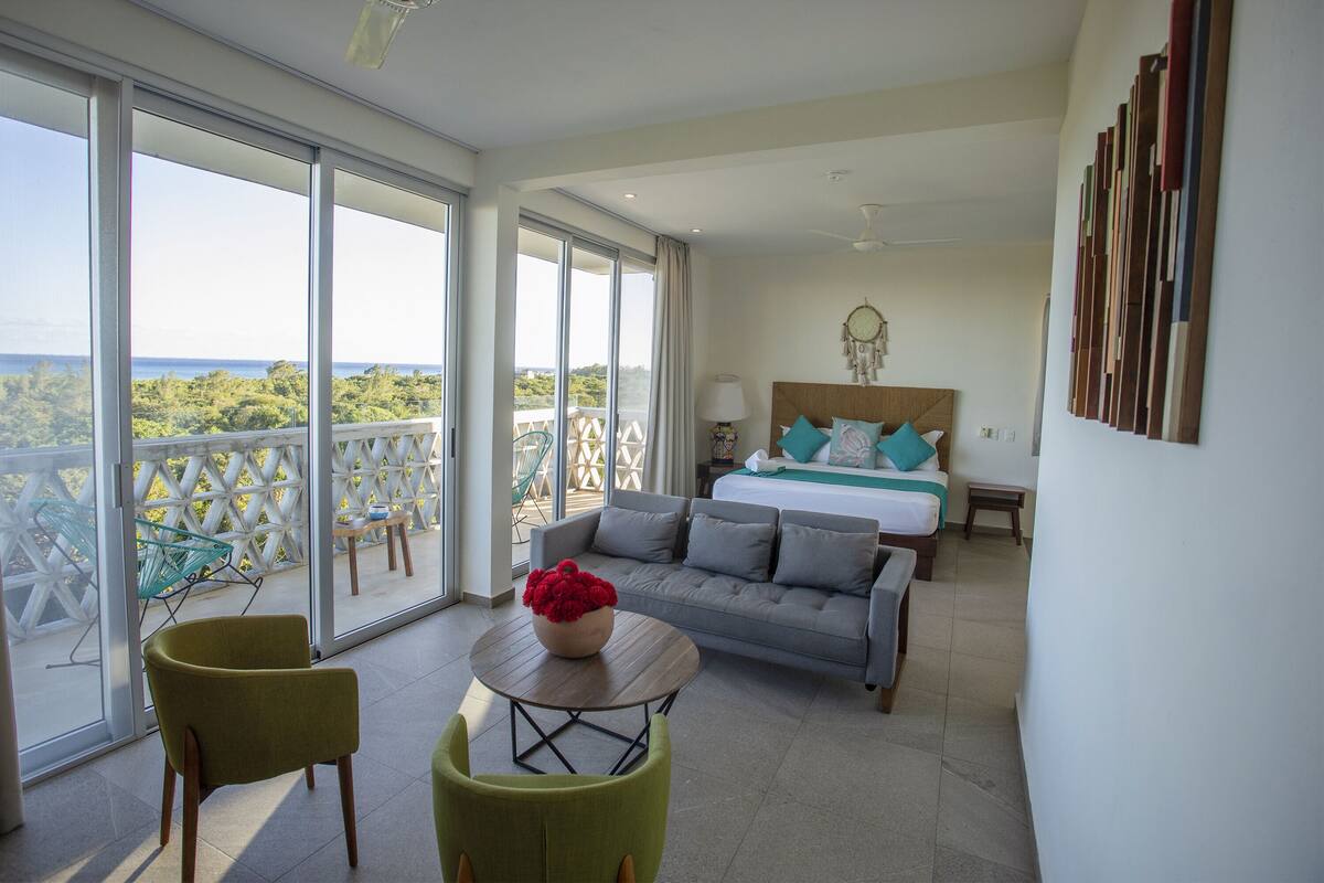 Une pièce spacieuse avec un balcon, un lit avec une literie bleue et blanche, et un fauteuil vert.