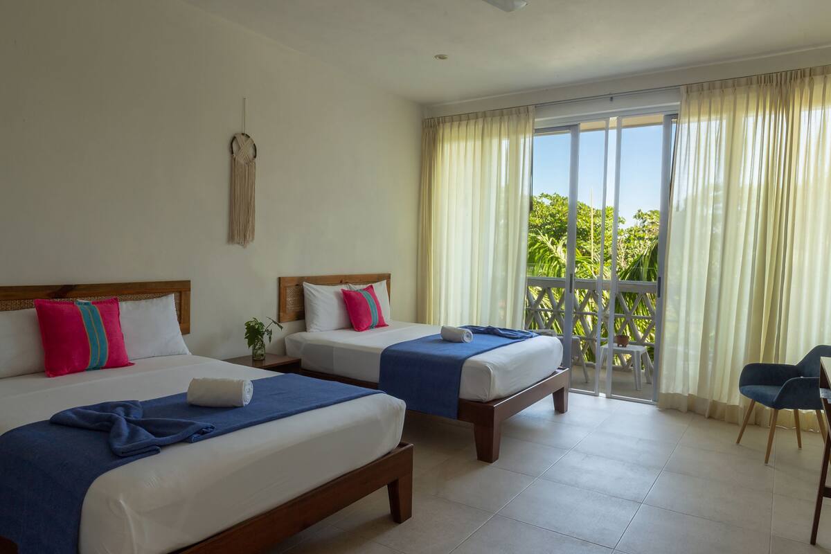 Une chambre d’hôtel avec deux lits, un balcon avec des rideaux et une chaise.