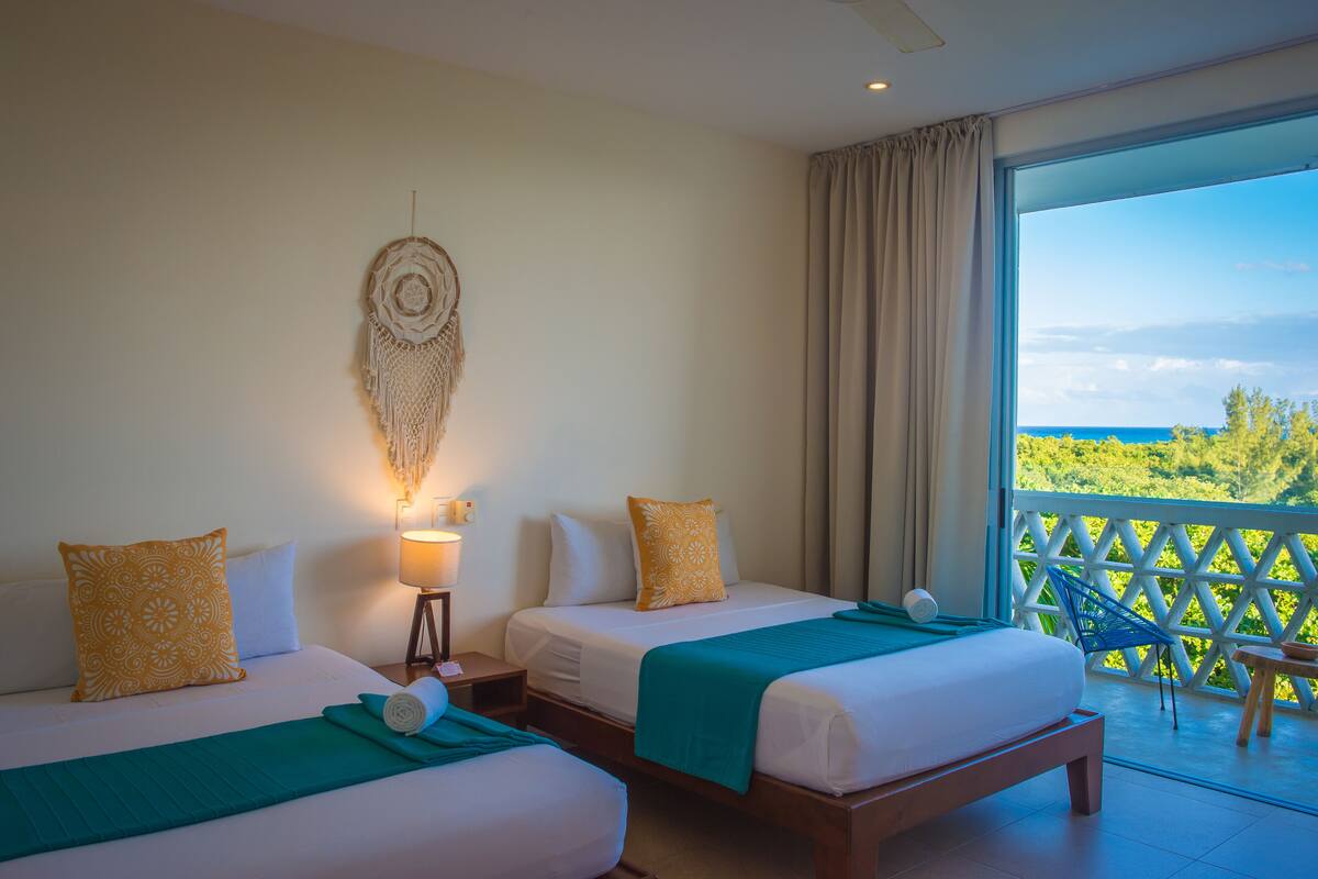 Une chambre d’hôtel avec deux lits, une grande fenêtre donnant sur un beau paysage, une décoration murale et un balcon avec vue.