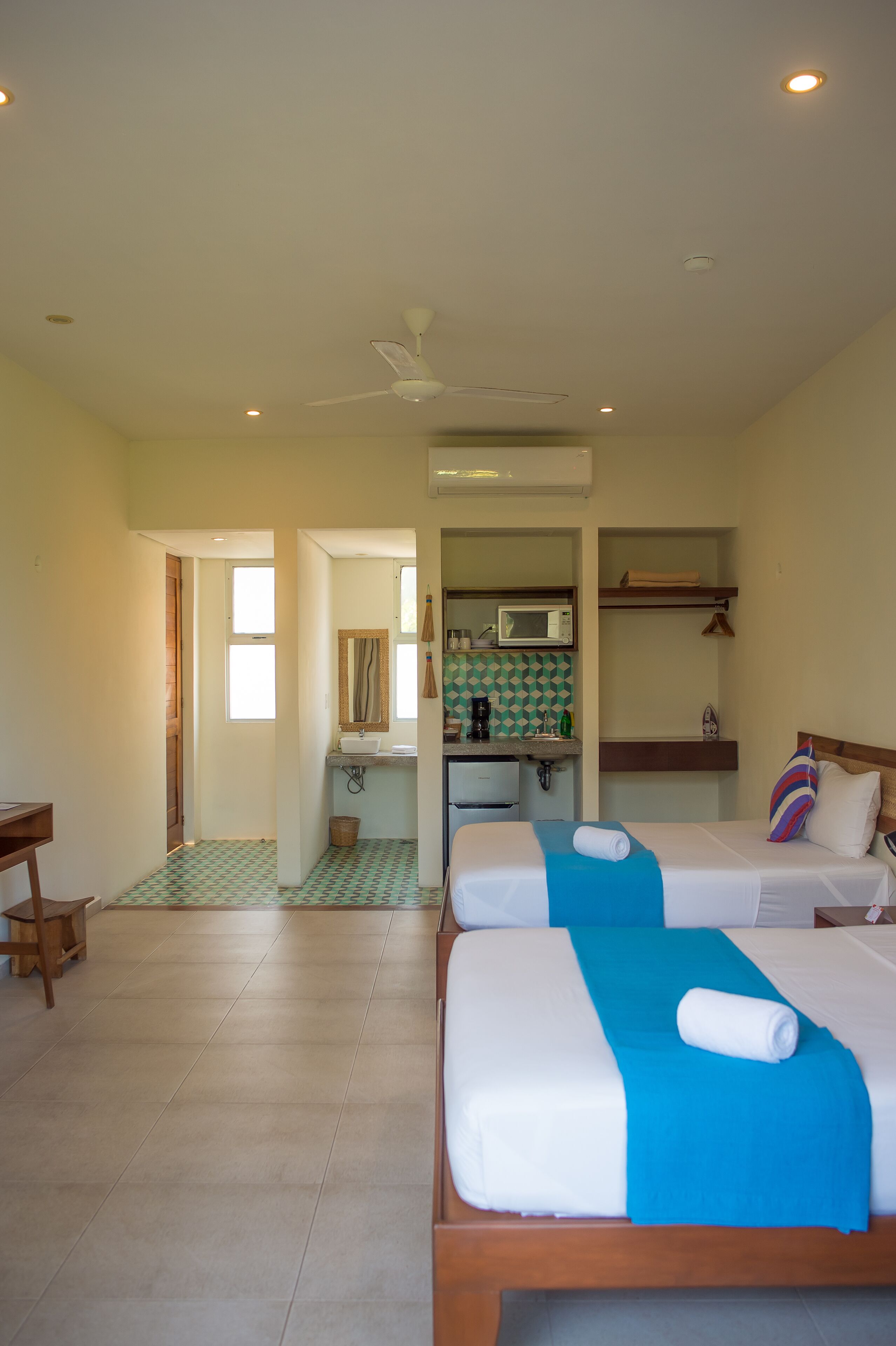 A hotel room with two beds, a bathroom, and a kitchenette.
