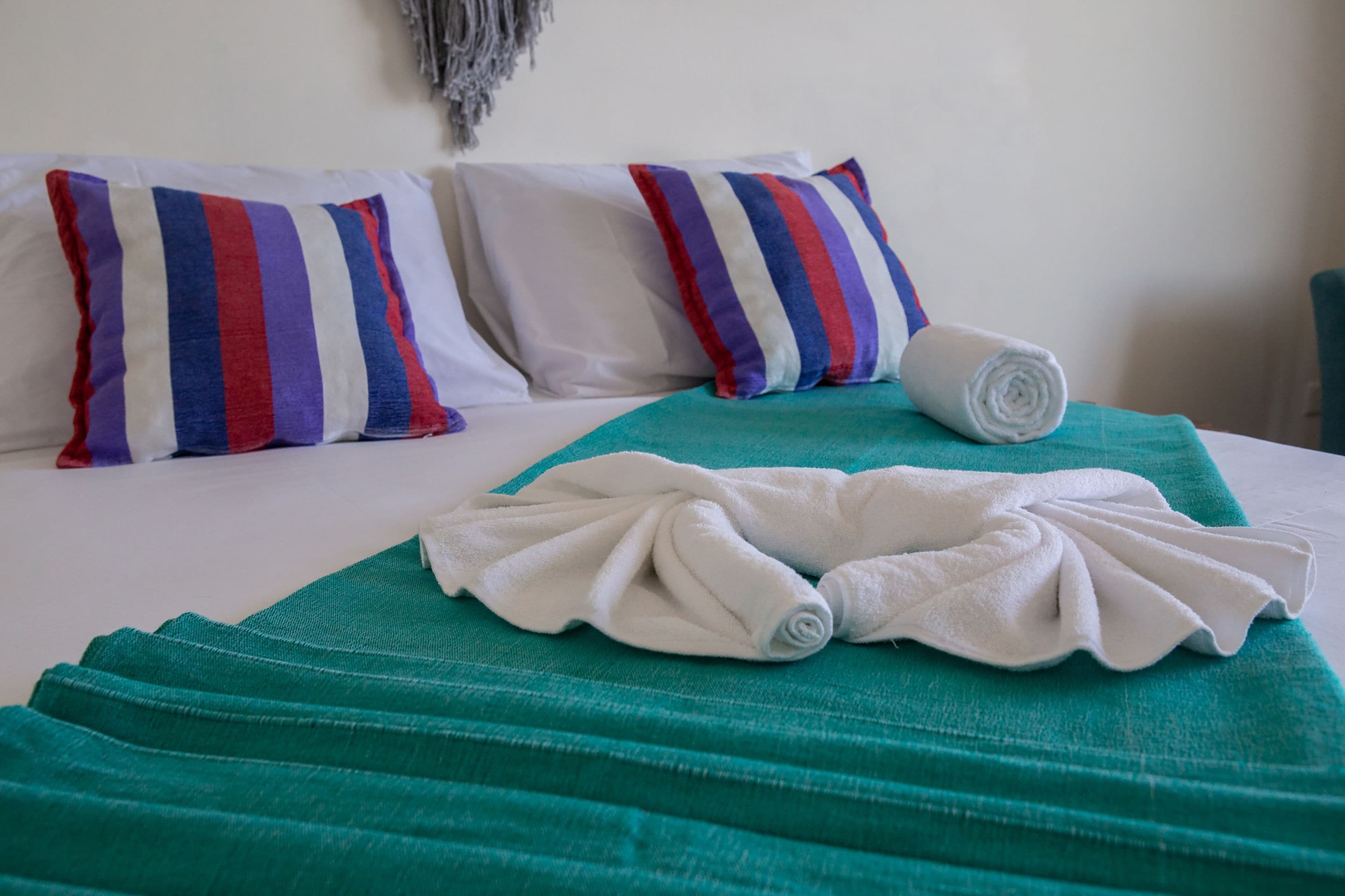 Una habitación de hotel con una cama, almohadas a rayas, una manta verde y toallas enrolladas.