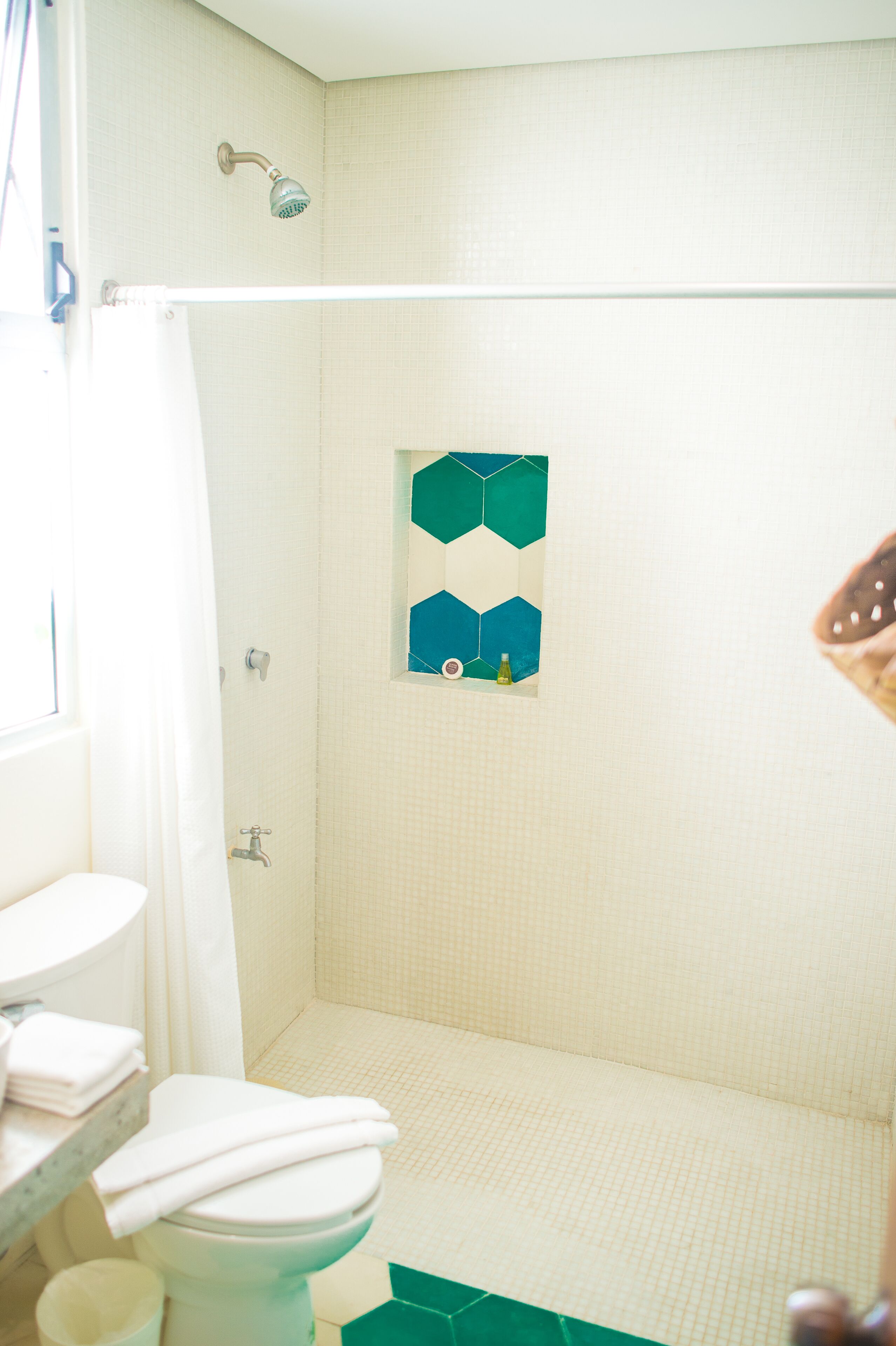 A bathroom with a shower, toilet, and a window.