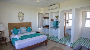 A modern hotel room with a large bed, a small table, a sofa, and a bathroom visible through an open door. - Suites Cielo y Mar (Playa del Carmen)