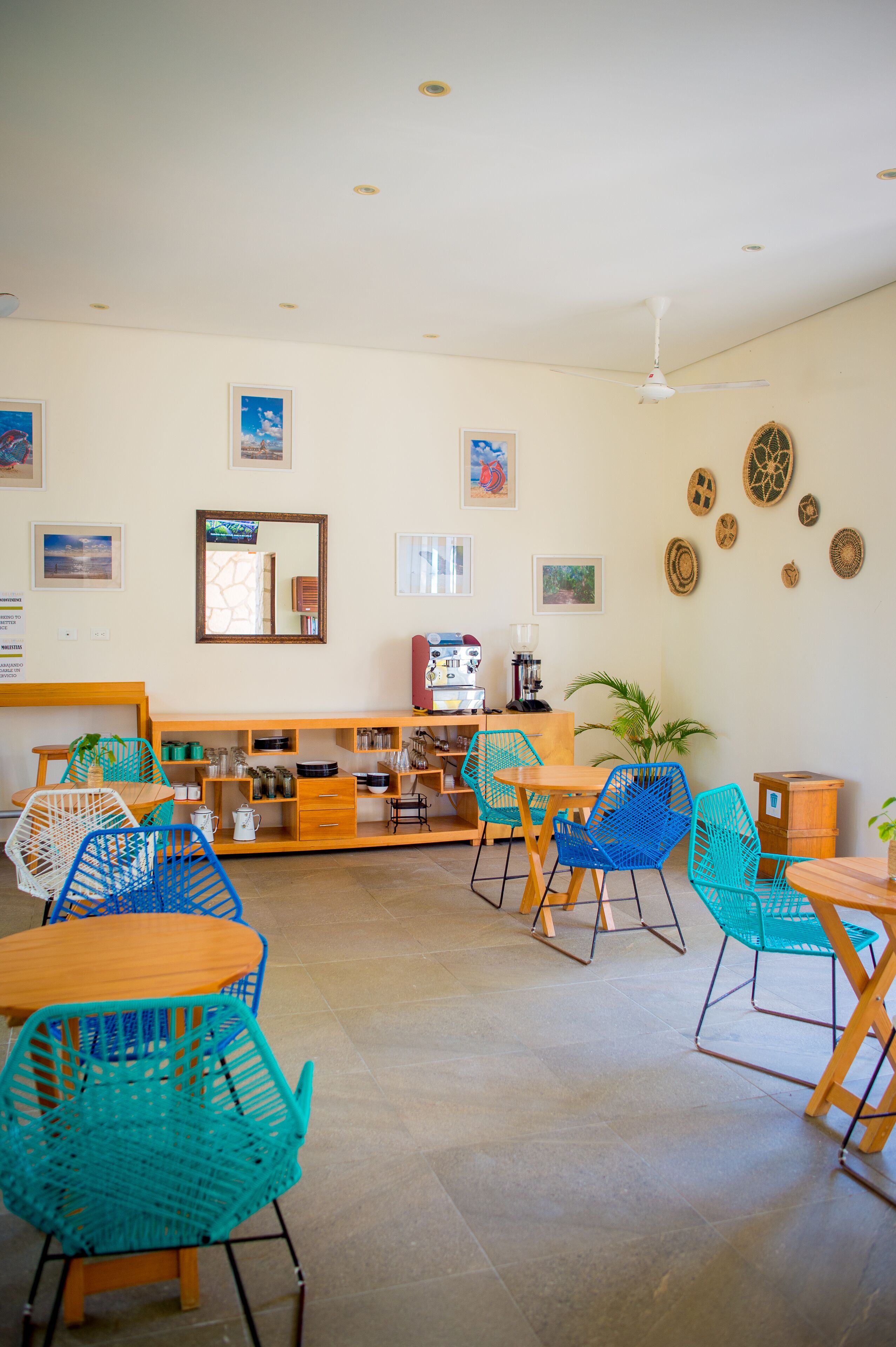 Una stanza spaziosa con una scrivania in legno, sedie blu, una macchina per il caffè e una ventola a soffitto.