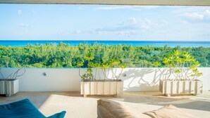 A balcony with a view of the ocean and greenery, featuring two potted plants and a beige sofa. - Suites Cielo y Mar (Playa del Carmen)