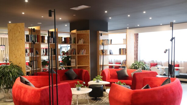 A modern lounge area with red sofas, a coffee table, and a bookshelf filled with books.