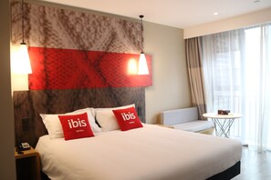 A hotel room with a large bed, two red pillows with "ibis Hotels" branding, a headboard with a marble-like design, a small round table, and a sofa. - ibis Chengdu SM Square (Chengdu)