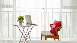 A room with a white table, a laptop, a potted plant, and a chair with a red pillow.