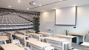 A classroom with rows of desks and chairs, a projector, a whiteboard, and a large screen.