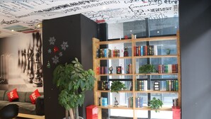 A modern interior with a bookshelf, a potted plant, and a sofa with red cushions.