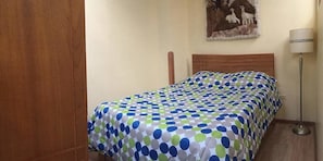 Een slaapkamer met een bed, overdekt met een sprei met stippen, een houten hoofdbord, een aan de muur hangend schilderij en een vloerlamp.
