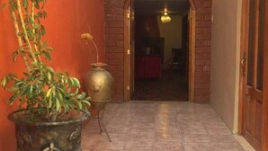 A hallway with a potted plant, a brass water dispenser, and a wooden door. - Casa Riso Cusco I (Cusco)