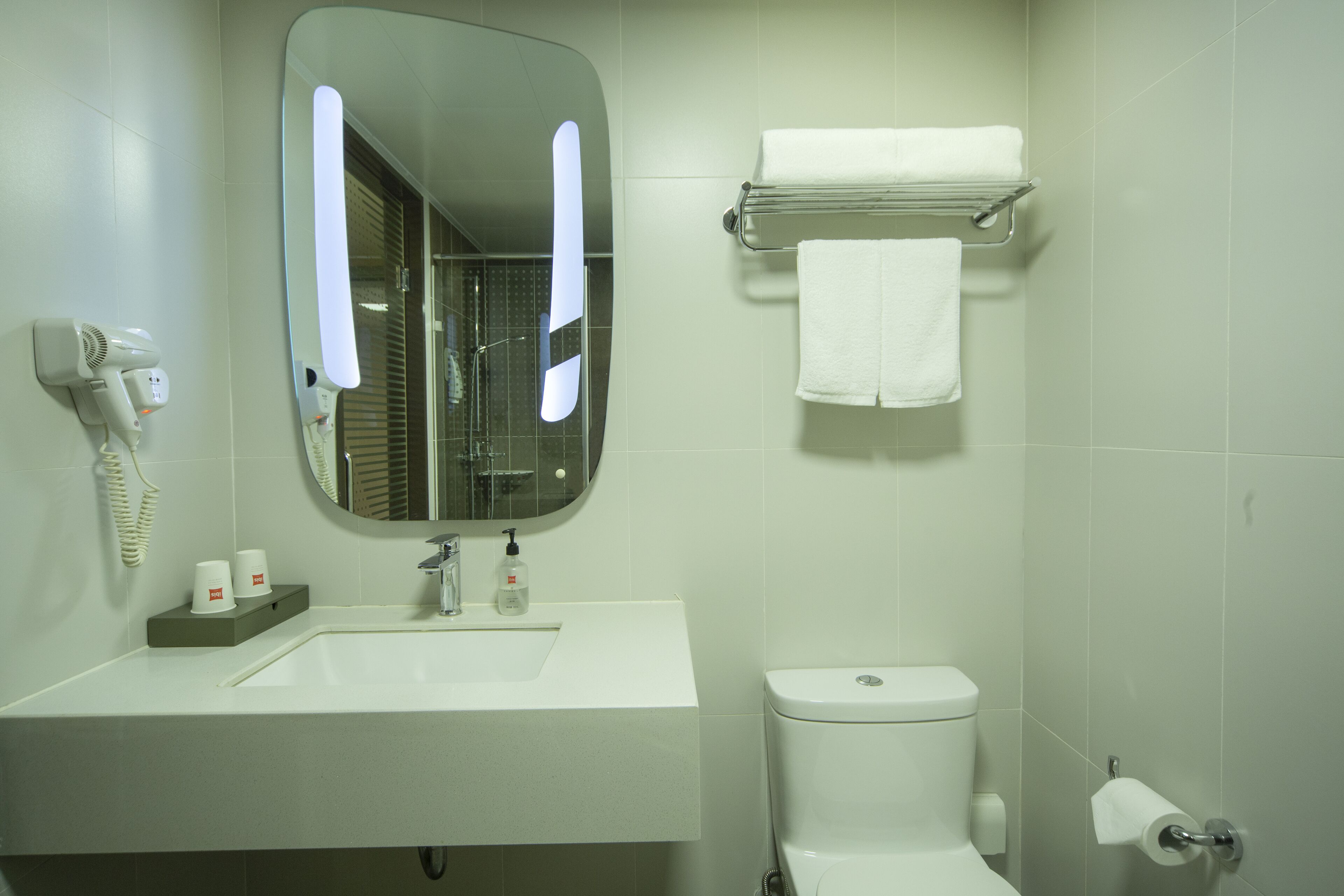 Un baño con lavamanos blanco, un espejo, toallero, inodoro y secador de pelo.
