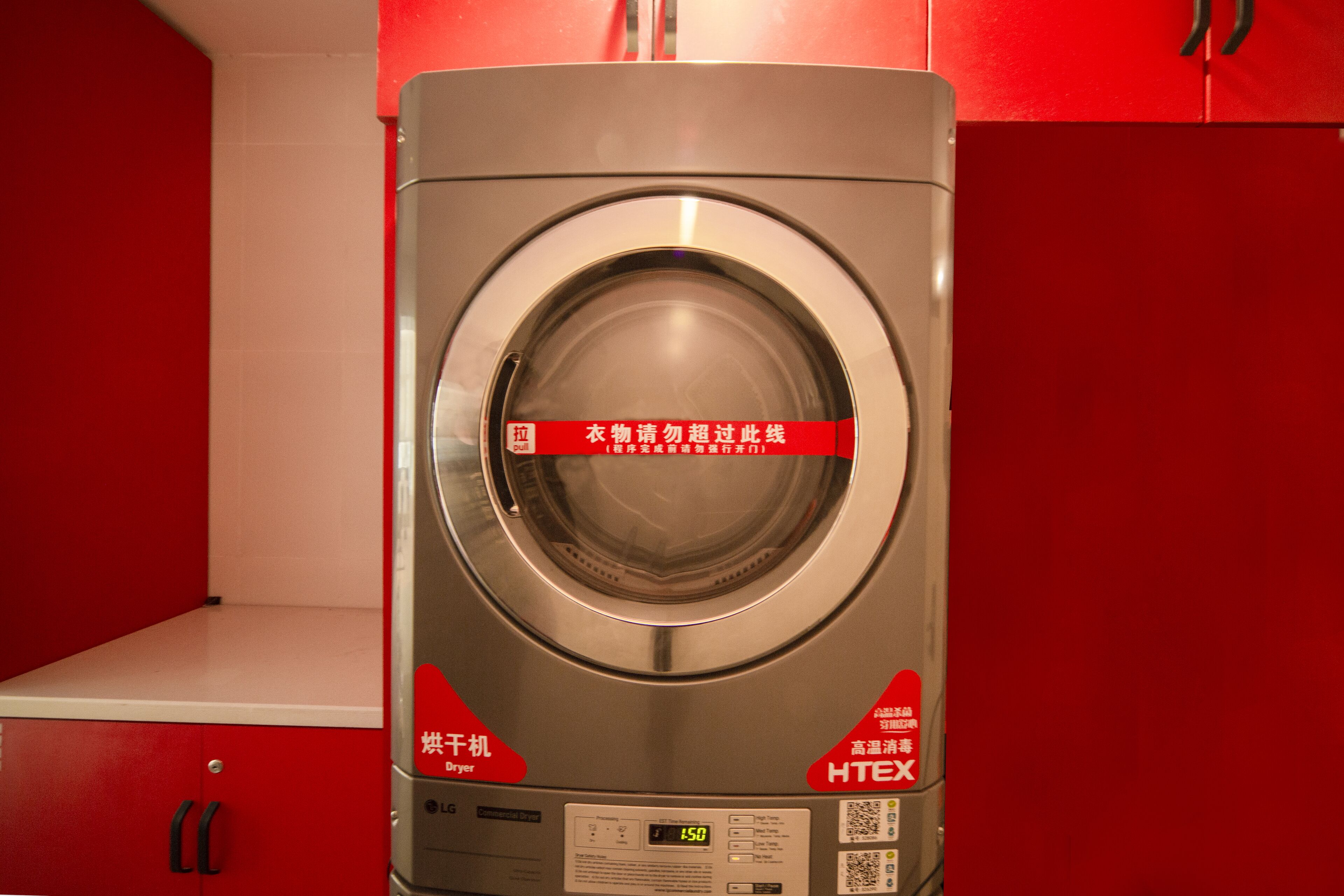 A front view of a silver, stainless steel front-loading washing machine with a digital display and control panel, placed against a red background.