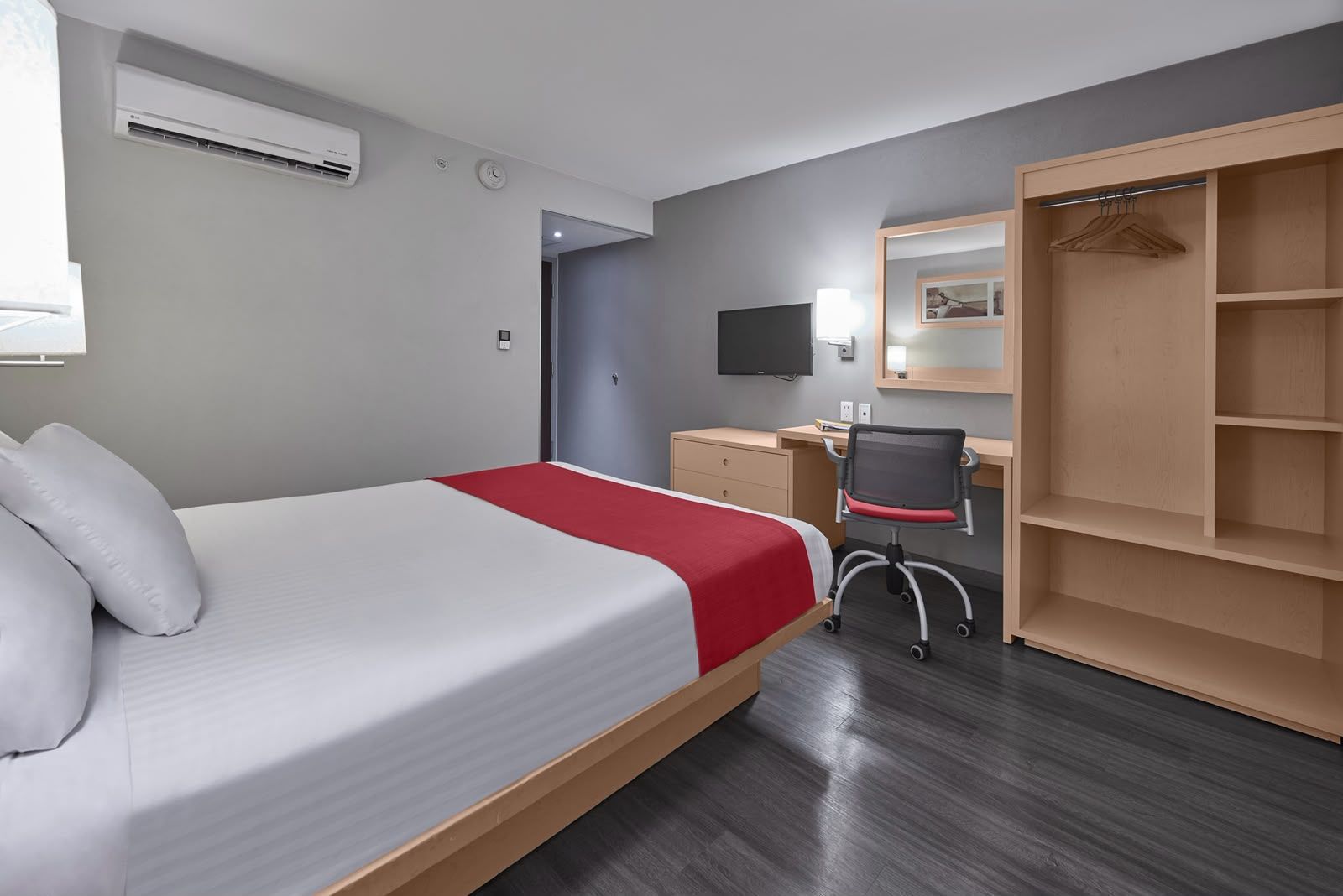 A hotel room with a bed, a desk, a chair, a wardrobe, and a television.
