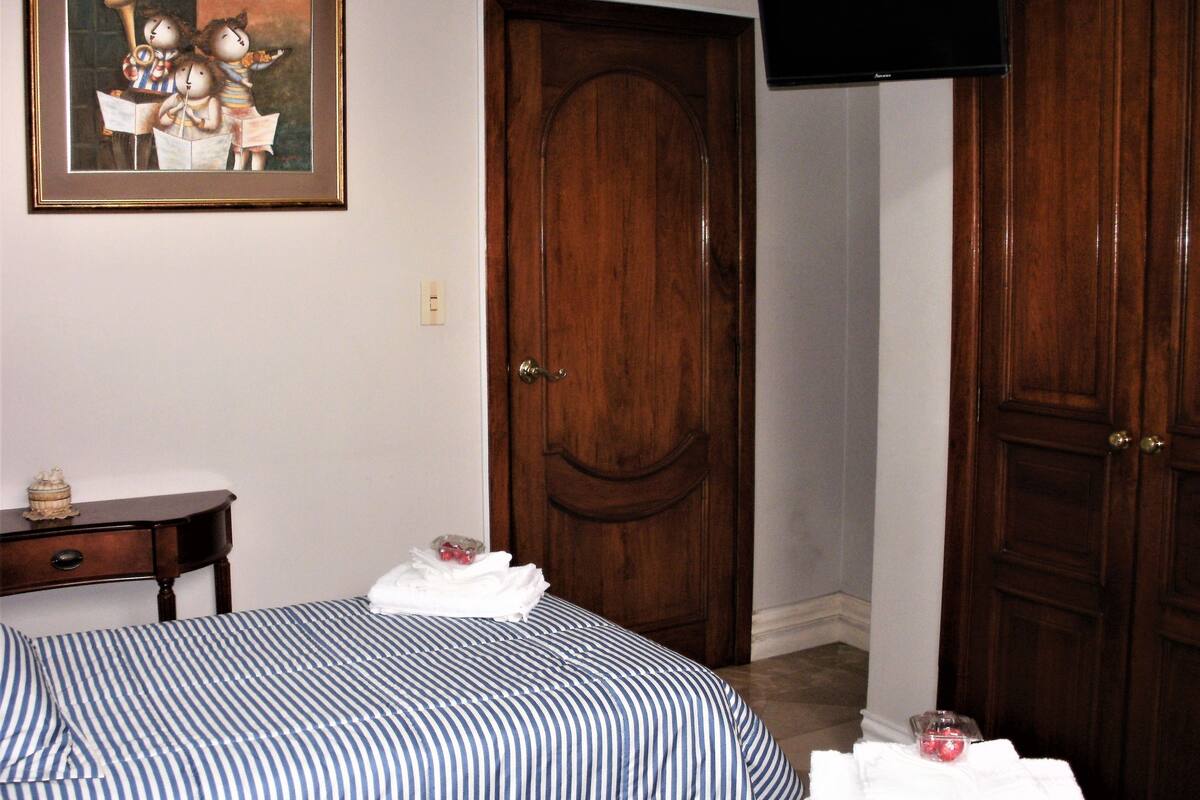 A bedroom with a large bed, a wooden door, a small table, and a framed picture on the wall.