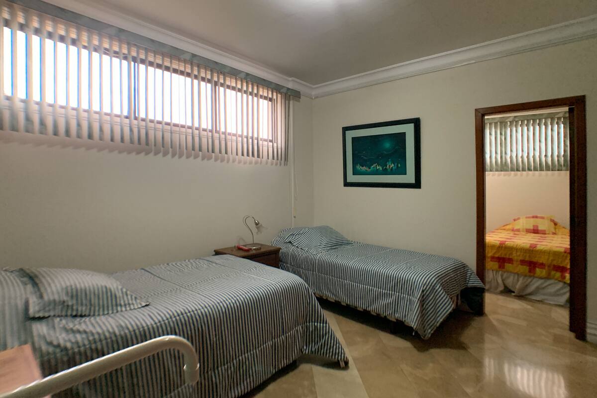 A room with two single beds, a nightstand, a framed picture on the wall, and a window with blinds.