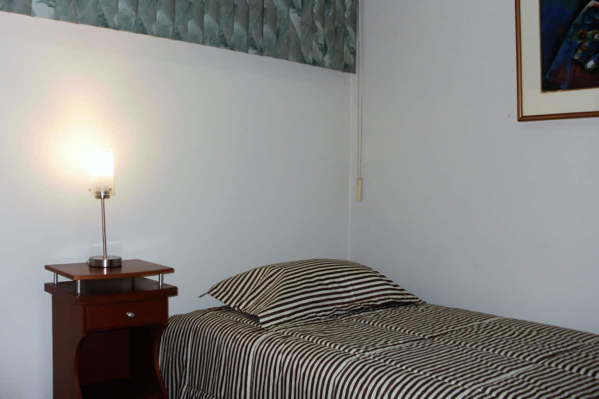 A bedroom with a bed, a nightstand, a lamp, and a painting on the wall.