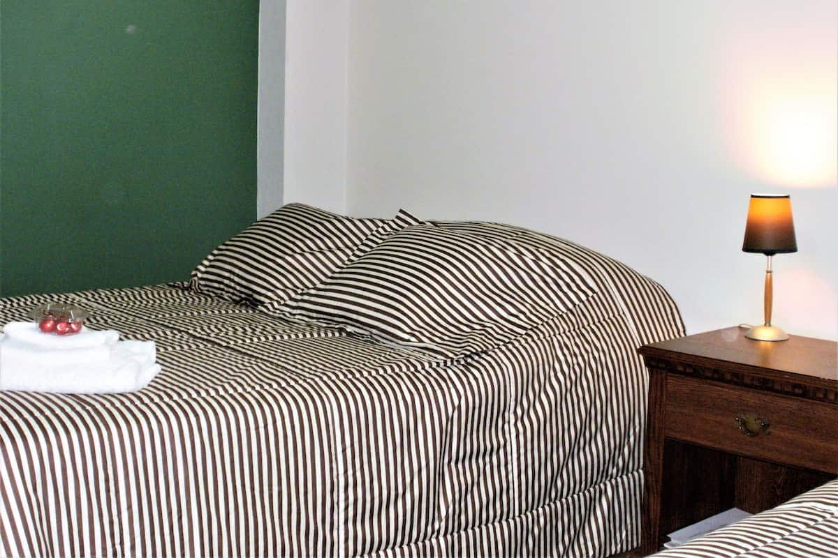 A bed with striped bedding, a bedside table with a lamp, and a small bowl of fruit on the bed.