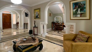 A spacious living room with a marble floor, a coffee table, a sofa, and a fireplace. There are framed artworks on the walls and a large mirror above the fireplace. - Cesar's House Guayaquil (Guayaquil)