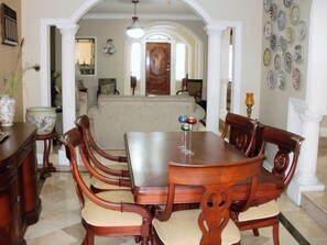 Un comedor con una mesa y sillas de madera, un candelabro y vista a una sala de estar con un sofá y placas decorativas en la pared.
