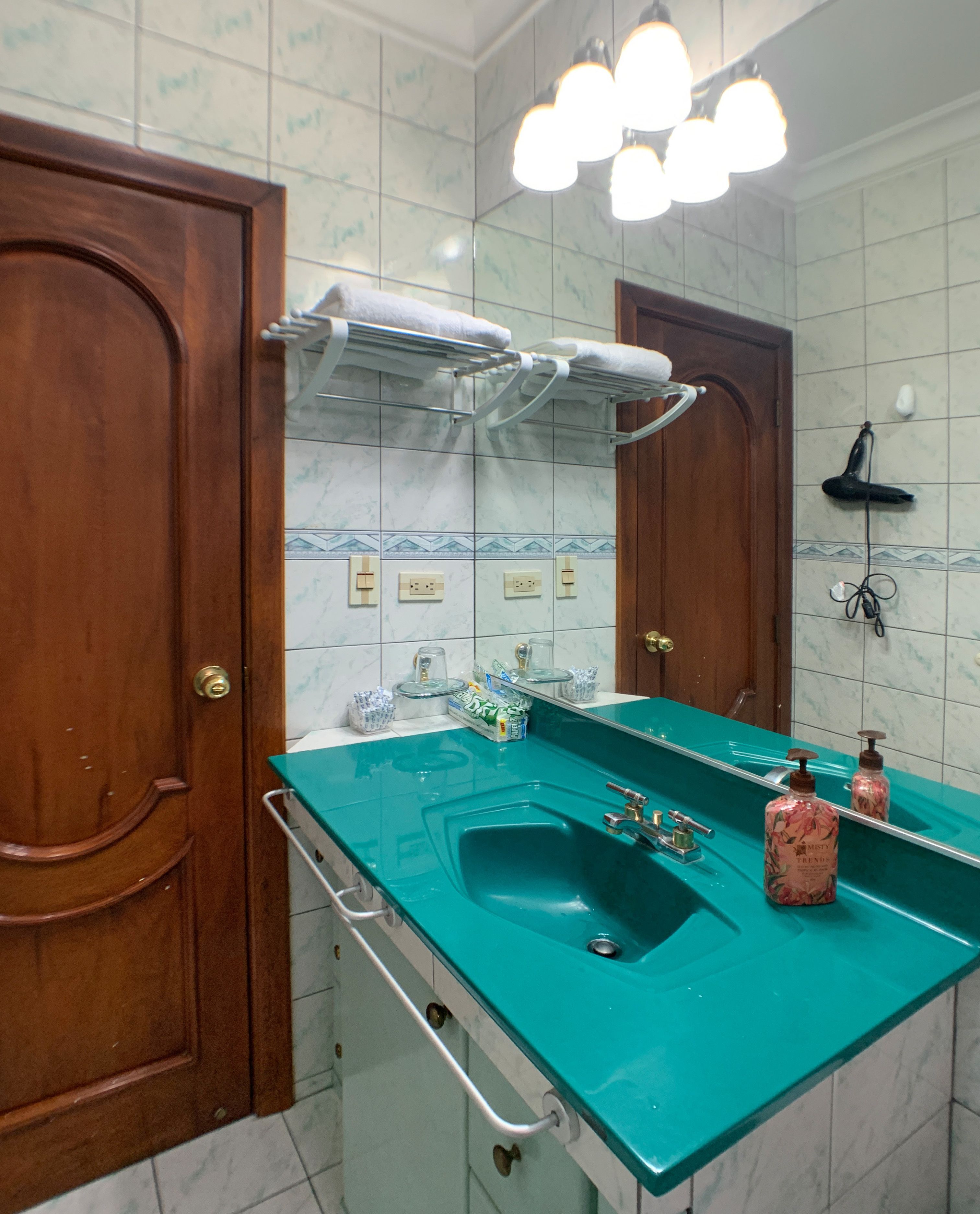 A bathroom with a teal sink, wooden doors, and a mirror with a light fixture above it.