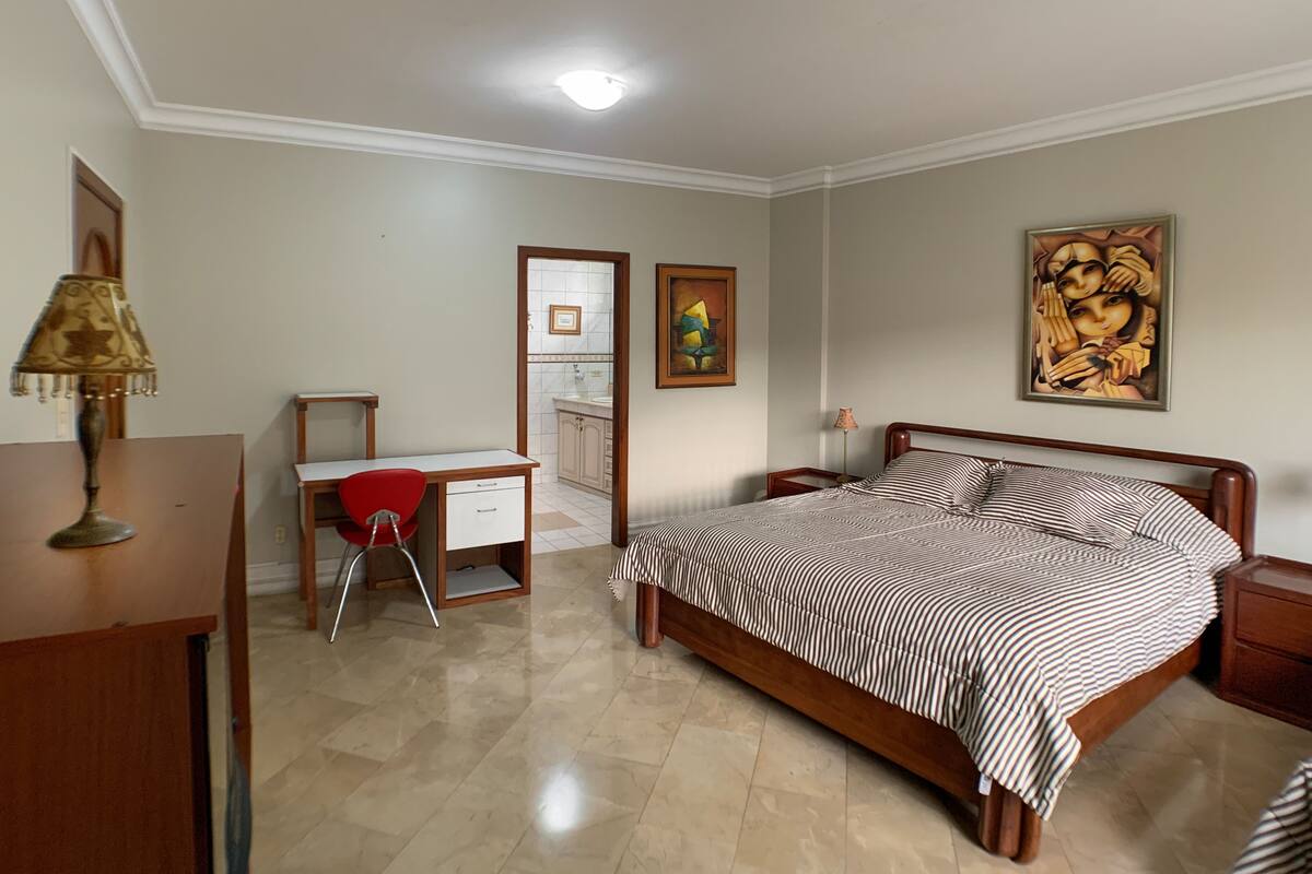 A bedroom with a bed, a desk, a chair, and a nightstand.
