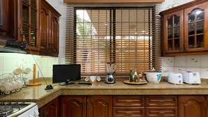 A kitchen with wooden cabinets, a gas stove, a blender, a toaster, and a window with blinds. - Cesar's House Guayaquil (Guayaquil)