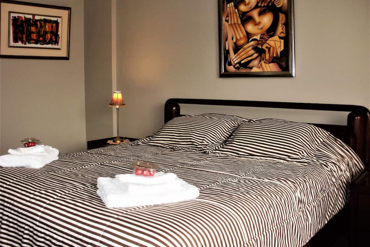 A neatly made bed with striped bedding, a framed artwork on the wall, and a bedside lamp.