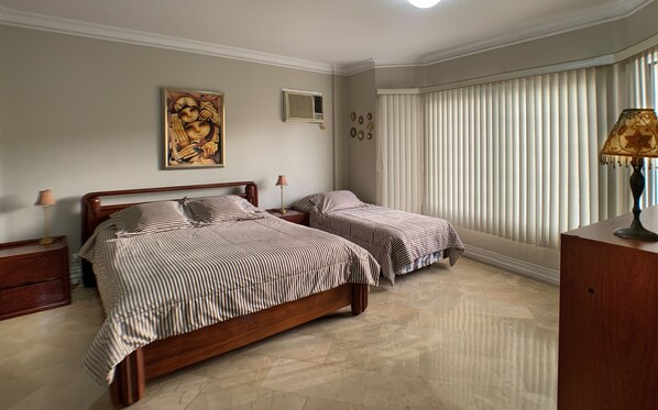 Un dormitorio con dos camas, una mesita de noche, una lámpara y una ventana con persianas.