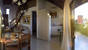 Un vaste espace de vie comprenant une table et des chaises en bois, un escalier menant à un autre niveau, une cuisine avec un dosseret carrelé et un balcon offrant une vue dégagée.