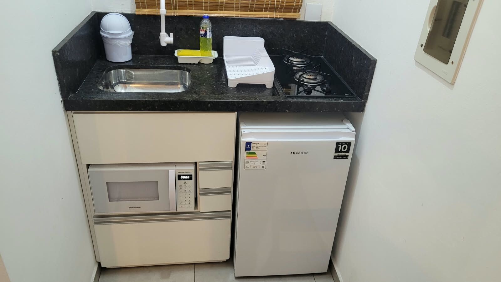 Eine kompakte Küche mit Mikrowelle, einem Hisense-Kühlschrank, einer Spüle und einem Gasherd.