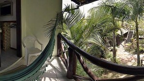 Un hamac sur un balcon, avec vue sur des palmiers et un mur de briques.