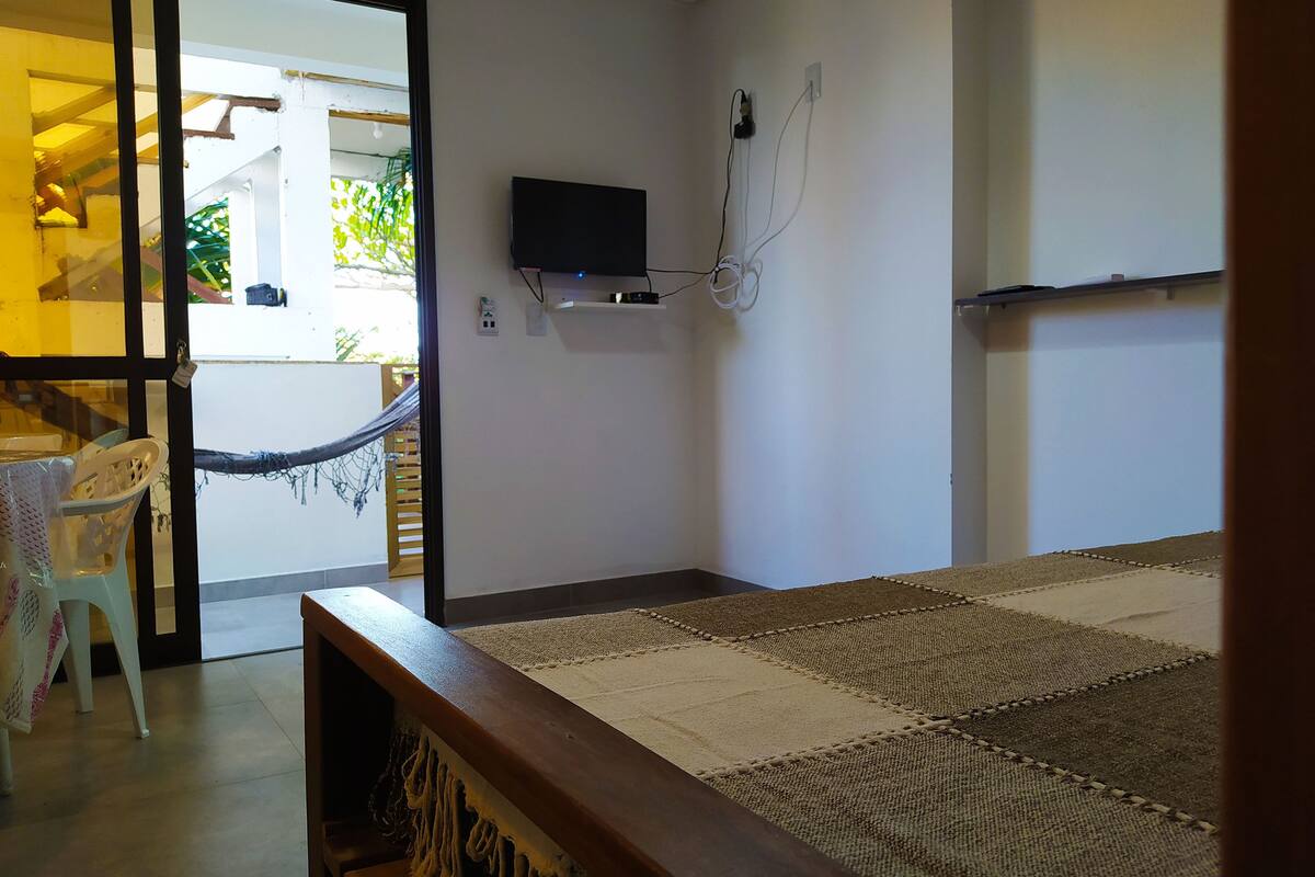 Ein Zimmer mit einem Bett, einem an der Wand befestigten Fernseher, einer Hängematte und Blick ins Freie.