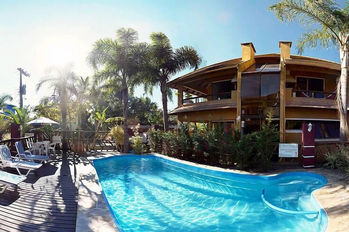 Ein Pool mit Liegestühlen und Palmen, umgeben von einer Holzterrasse und einem zweistöckigen Gebäude.