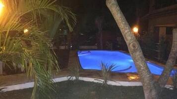 A nighttime view of a swimming pool surrounded by trees and a building.